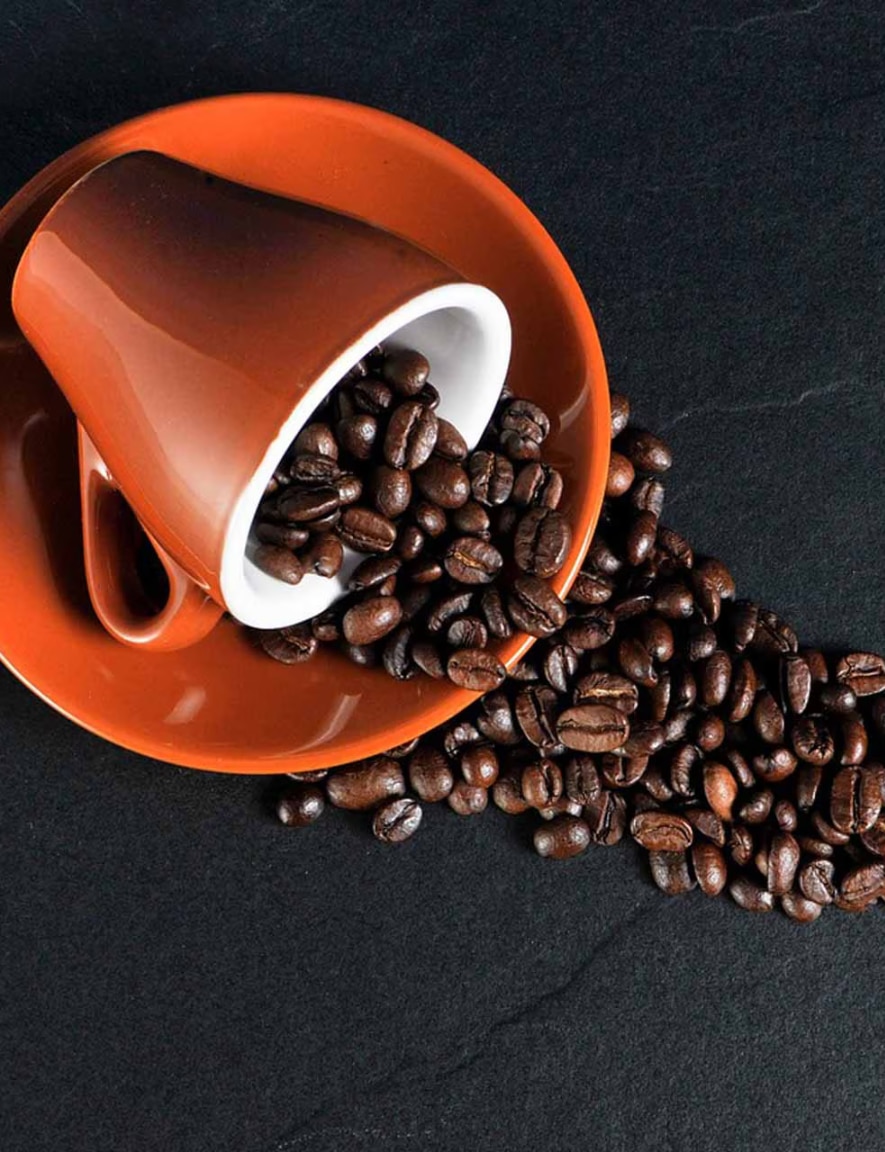 Dark orange cup full of coffee beans spilled on its side