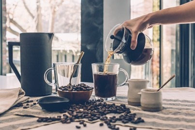Coffee being poured into a mug surrounded by coffee beans