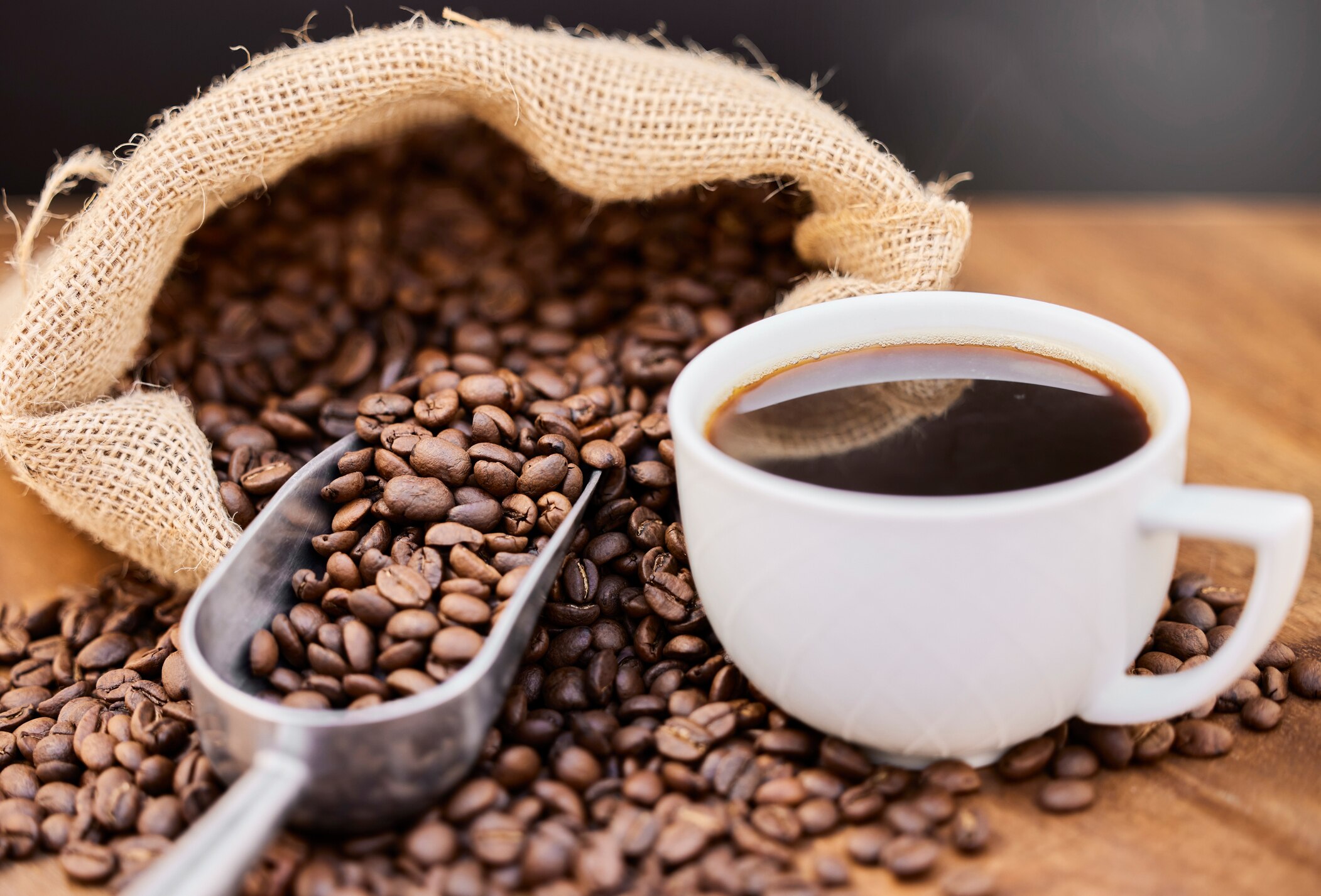 Coffee beans spilling out of a coffee sack next to a mug of coffee